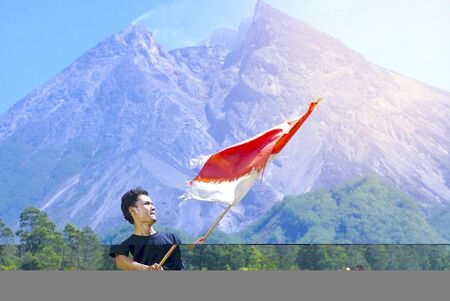 A man stand with Indonesia flag stands with Merapi Mt background. indonesia independence day celebration conceptの写真素材