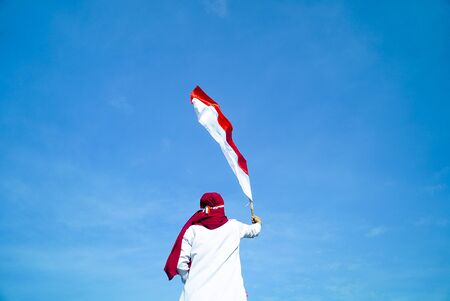 Asian Hijab flapper Indonesian flag with clear blue sky background, Indonesia independence dayの写真素材