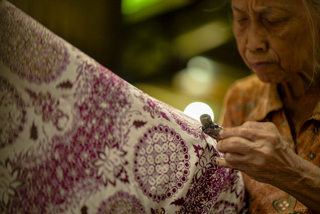 August 11 2019, Surakarta Indonesia : Woman Making Batik with Close Up hand to make batik on the fabric using canting with bokeh backgroundのeditorial素材