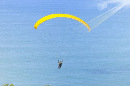 Paraglider tandem flying over the sea with blue water and mountains in bright sunny day, Summer Holidayの写真素材