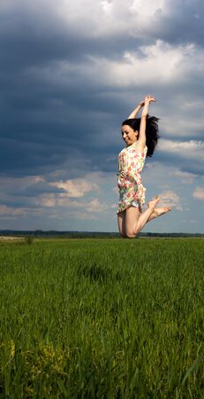 young girl jumping on the field on sunny summer dayの写真素材