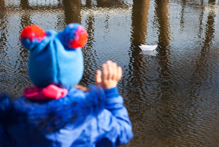girl waving a paper boat floating in the creek on spring dayの写真素材