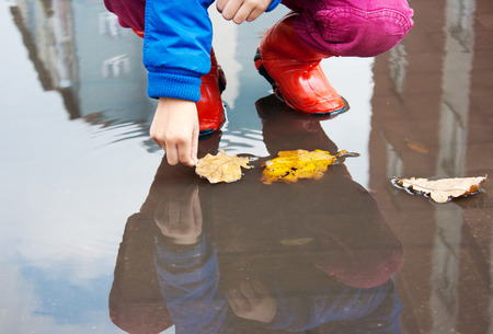 little girl in red rubber boots holding yellow leaf in a puddle closeupの写真素材