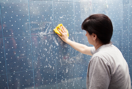 woman in a gray shirt washes blue tile with a cloth with soapy foam in the bathroomの写真素材