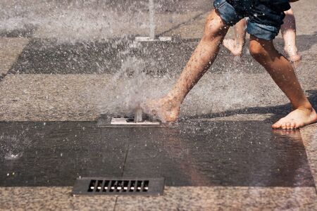 boy's feet in blue jeans playing in the fountain on summer day closeupの写真素材