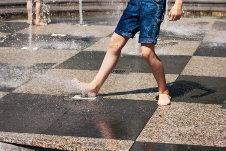 feet of boy in blue jeans playing in the fountain on sunny summer dayの写真素材
