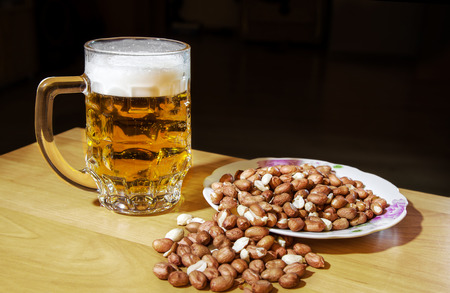 mug of beer and peanuts on the wooden table closeup