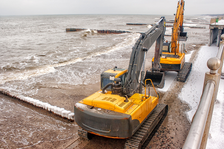 two excavators riding on the beach on winter cold dayの写真素材
