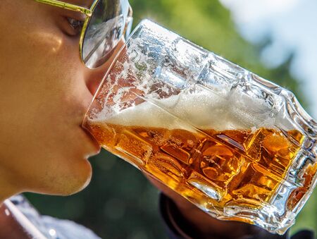 young man drinking beer from mug outdoor on sunny summer day closeup