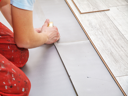 handyman laying down laminate flooring boards while renovating a house. hands closeupの写真素材