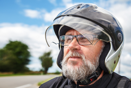 portrait of elderly motorcyclist wearing a jacket and glasses with a helmet on sunny summer day outdoor closeupの写真素材