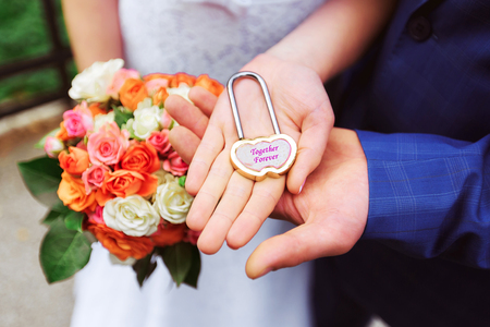 hands of the bride and groom holding a padlock closeupの写真素材