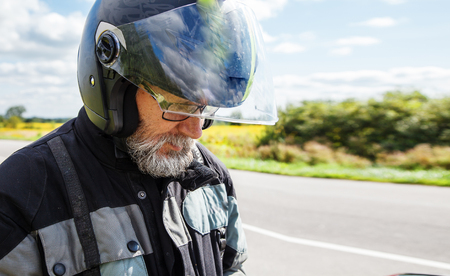 portrait of elderly motorcyclist wearing a jacket and glasses with a helmet on sunny summer day outdoor closeupの写真素材