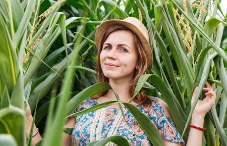 portrait of a young smiling woman in a straw hat in a corn field on sunny summer dayの写真素材