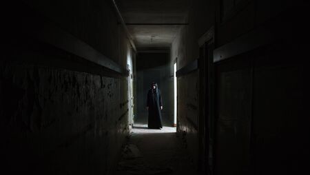 gothic brunette woman standing in long corridor of dark gloomy abandoned house