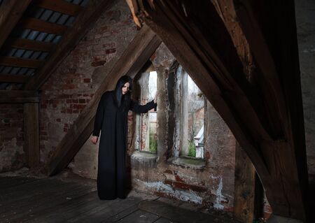gothic brunette woman standing near the window in attic of dark gloomy abandoned houseの写真素材