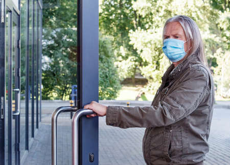 elderly man in protective mask opens the door to the store outdoor on autumn day