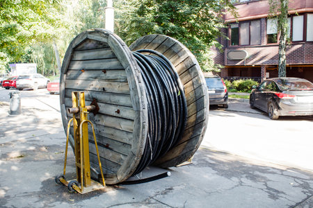 large wooden spool with cable prepared for laying on city street on sunny summer day