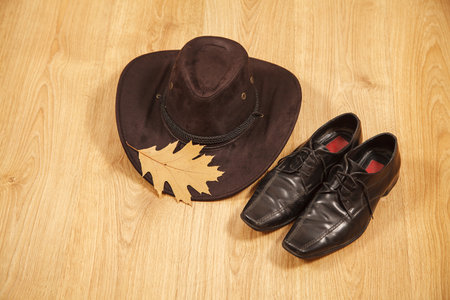 set of men's felt hat with a yellow maple leaf and black shoes on a wooden floorの写真素材