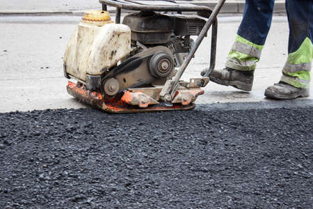 worker ramps the asphalt on the road with a mechanical rammer. laying the road surface. hot asphalt...