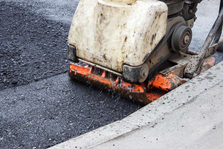 worker ramps the asphalt on the road with a mechanical rammer. laying the road surface. hot asphalt...