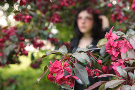 portrait of young beautiful brunette girl in black jacket and burgundy sweater standing near cherry blossoms on sunny spring day. outdoor closeupの写真素材