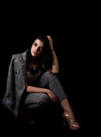 young beautiful girl in a business suit posing sitting on floor the studio on black backgroundの写真素材