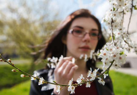 portrait of young beautiful brunette girl in black jacket and burgundy sweater standing near cherry blossoms on sunny spring day. outdoor closeupの写真素材