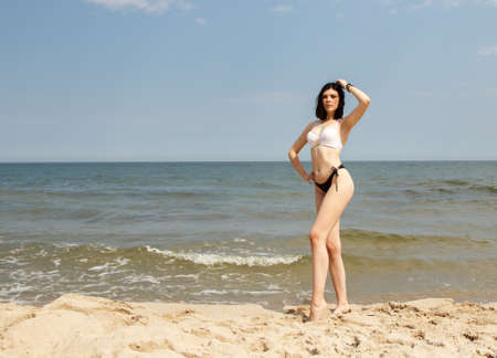 young brunette in bikini woman stands on the sand by the seaの写真素材