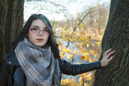portrait of young brunette girl in black jacket in city park on an sunny autumn day