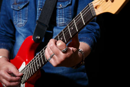 elderly man in blue denim shirt plays the electric guitar on black background. hands closeup