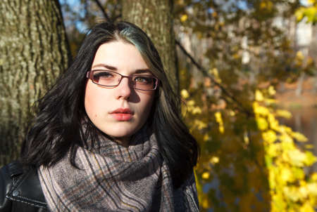 portrait of young brunette girl in black jacket in city park on an sunny autumn dayの写真素材