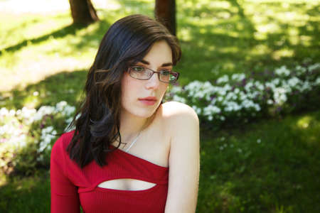 young brunette woman in a red dress and glasses in city park on sunny summer day. portrait closeupの写真素材