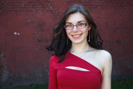 portrait of pretty brunette young woman in red dress and glasses in city park on summer dayの写真素材