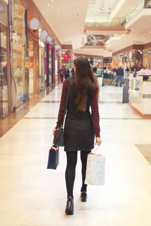 Woman is walking in the shopping center, back of the shopping girl with shopping bags in interior of the mallの写真素材