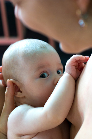 Newborn baby with cute expression is sucking mother's breast, hungry infant breastfeeding close upの写真素材
