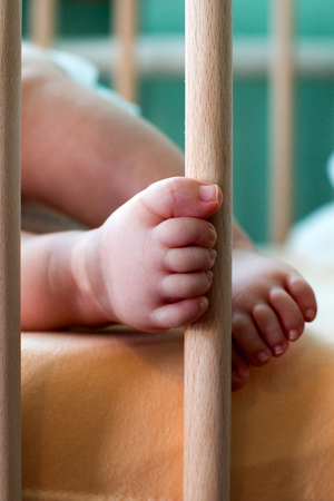 Infant little toes touching the wooden pose of the baby crib, beautiful Infant feet lying on the bedの写真素材