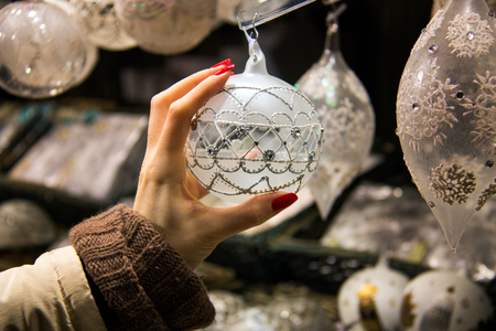 Pretty hand reaching and grabbing Christmas decoration, beautiful ornamental Christmas design, shopping woman hand with long red nails touching luxury silver pearl  Christmas ball displayed in shopの写真素材