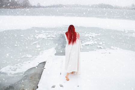 Back View red hair woman walking outdoors on the snow to the frozen frosty lake for the ice bath while snowing. Hardening in cold water, winter open water swimming and cryotherapy conceptの写真素材