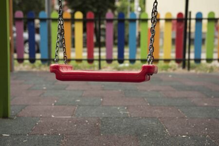 Swinging cradle for children in park. Playing concept. Fence painted in rainbow colors.の写真素材