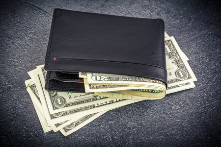 black leather wallet with banknotes lying on a rustic concrete background