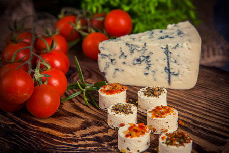 Cheese with spices and cherry tomatoes on a wooden board. Toned.