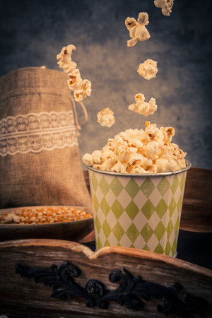Popcorn falling into a paper cup on vintage background. Toned.の写真素材