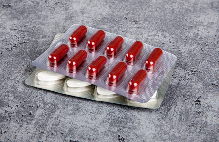 Red and white pills in blister pack on gray background. Copy space.