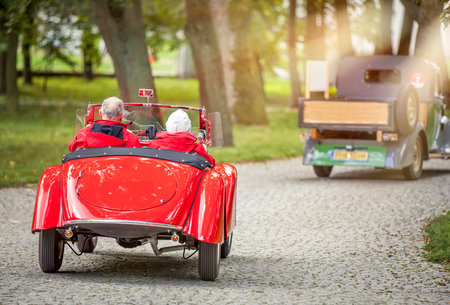 Rear view of senior couple driving a vintage race car on a country roadの写真素材