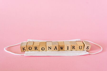 Koronawirus means coronavirus in polish, written with wooden letters on pink background, white face...