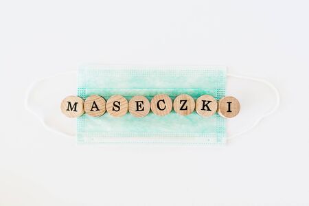 Words written with wooden blocks with black letters laying on protective surgical masks "Maseczki" means "masks" in polish.の写真素材