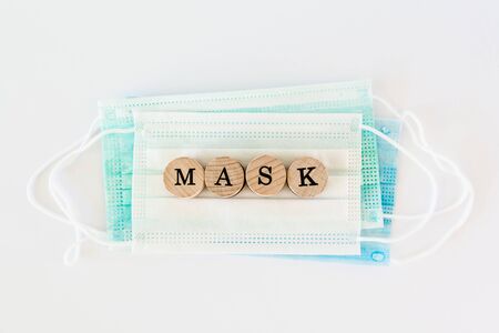 Word mask written with wooden blocks with black letters laying on protective surgical masks, flat lay conceptの写真素材