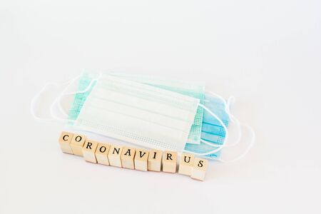 Word coronavirus written with wooden blocks with black letters isolated with a protective surgical...