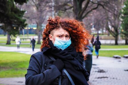Beautiful young European woman in spring clothes on the street with a medical face mask on. Closeup of a 30-year-old female in a respirator to protect against infection with coronavirus - Covid19の写真素材